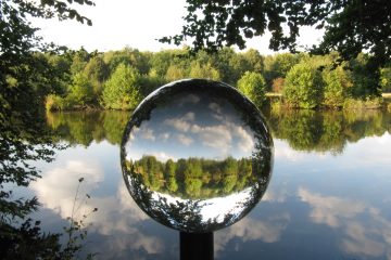 Ein blick in die Glaskugel wo sich Wasser, Bäume und Himmel spiegeln.