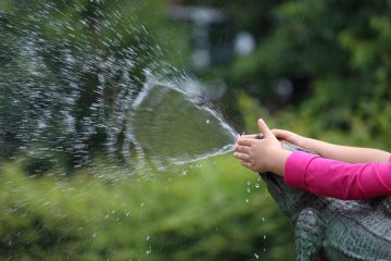 Kinderhände spielen mit einem Wasserstrahl.