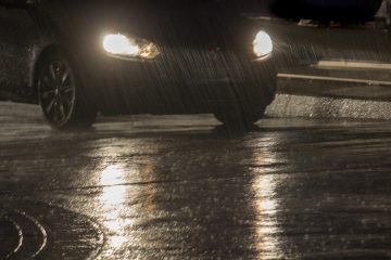 Nachts Im Regen ist ein Auto zu sehen, Scheinwerfer spiegeln sich auf nasser Straße.